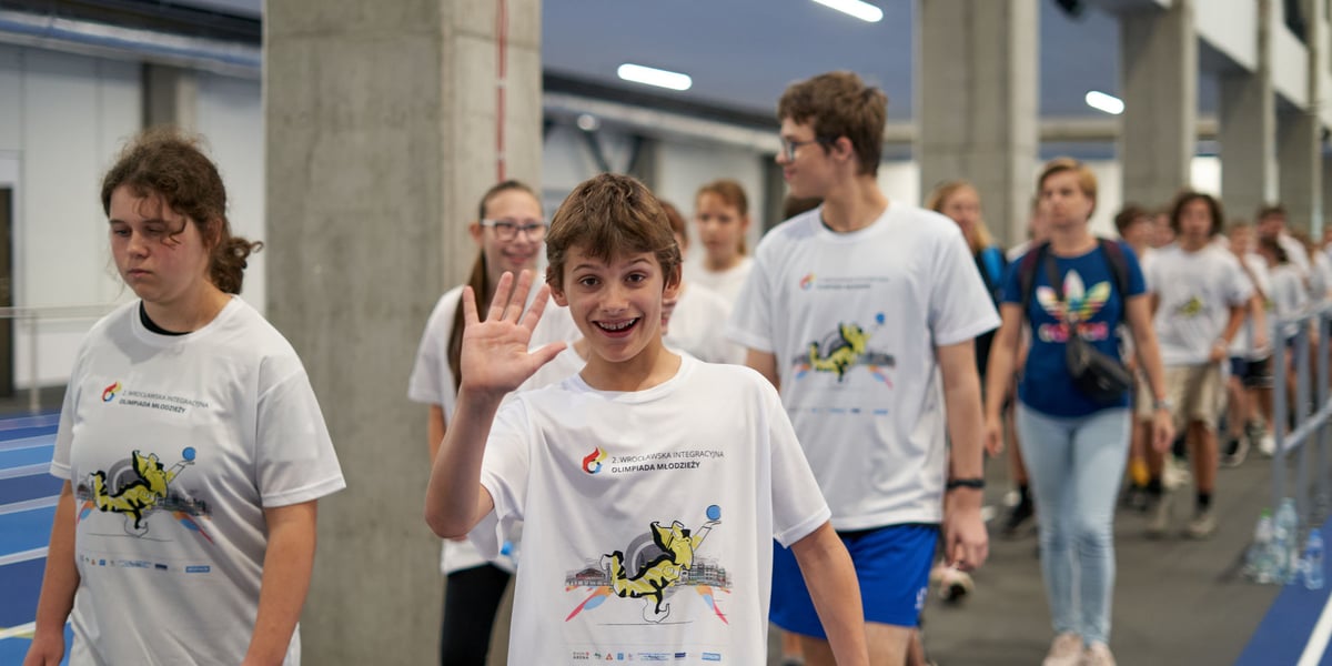 Uśmiechnięty chłopak unosi dłoń, idąc po bieżni w hali sportowej Ślęzy na Kłokoczycach