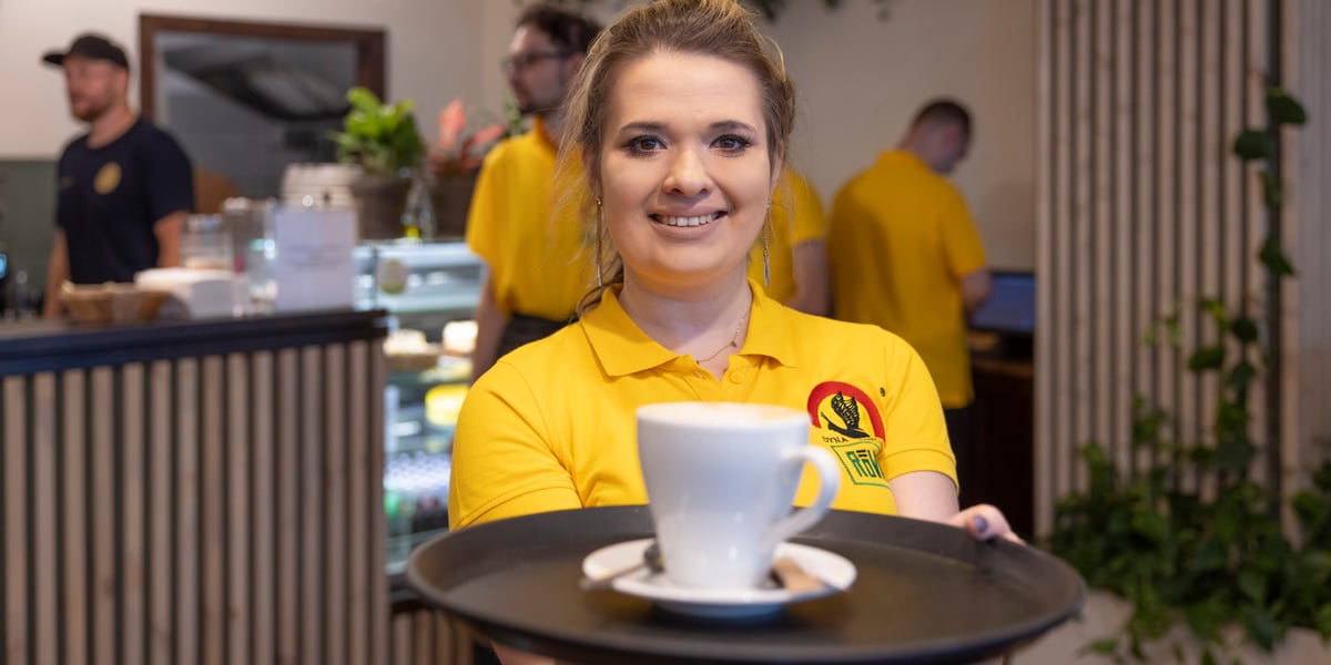 Cafe Równik po metamorfozie. Na zdjęciu uśmiechnięta kelnerka i baristka, w tle odmienione wnętrze.
