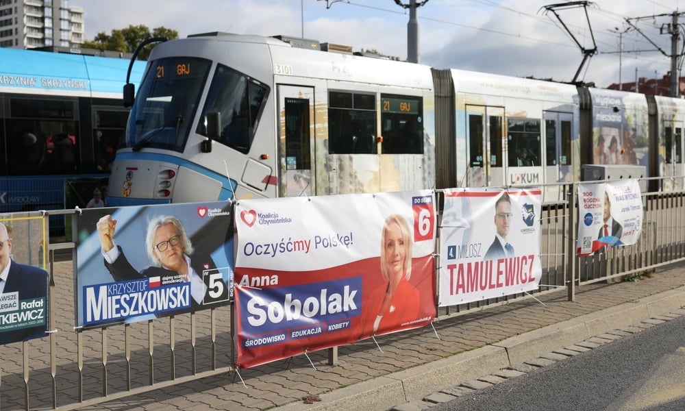 Plakaty wyborcze wiszące na płocie wzdłuż przystanku tramwajowego 