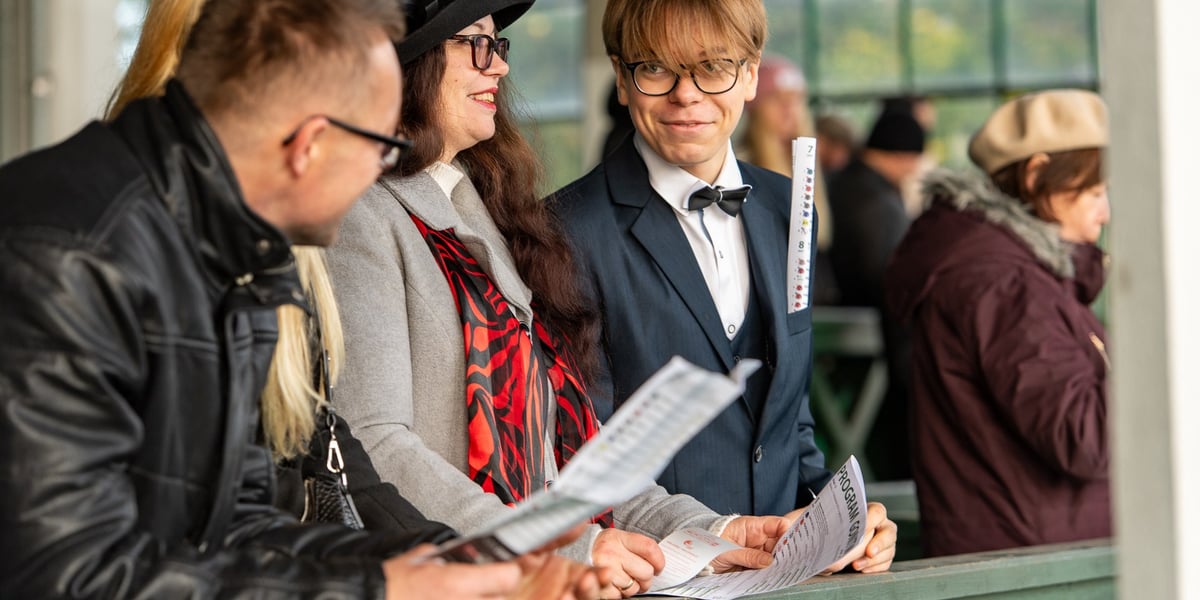 Widzowie z programami, oparci o barierę trybuny na torze wyścigów konnych podczas ostatniego dnia sezonu 2023