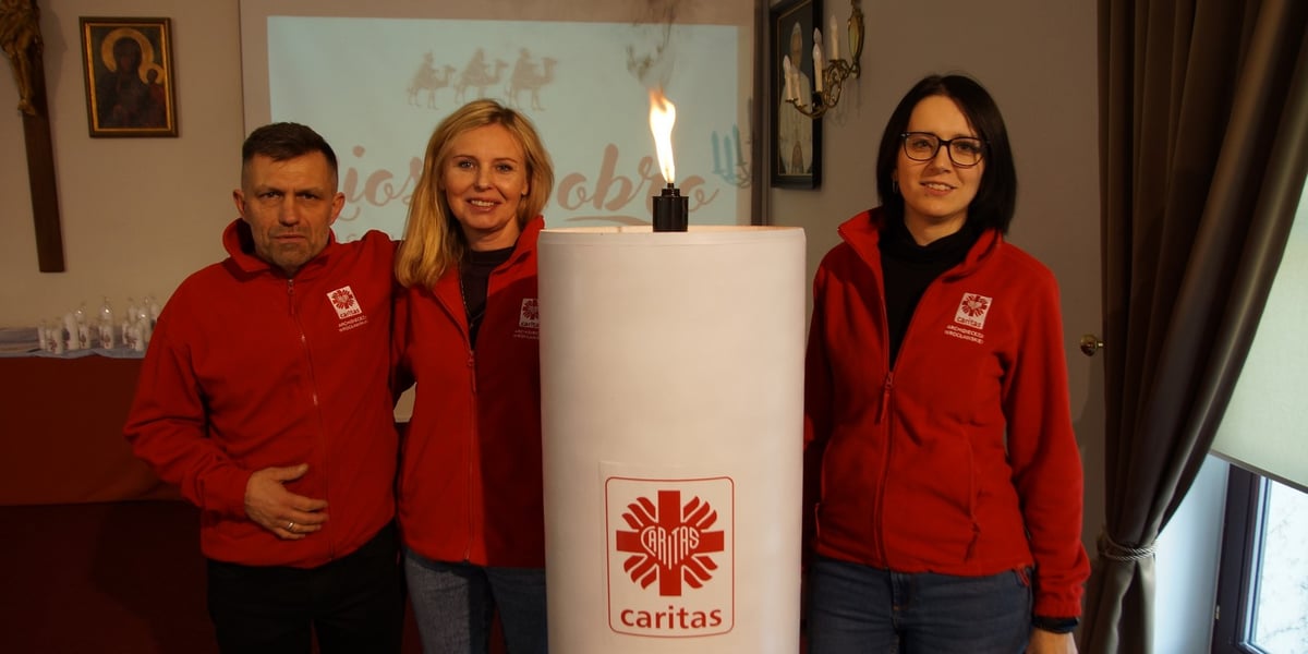 Wolontariusze Caritas obok wielkiej, jubileuszowej świecy wigilijnej