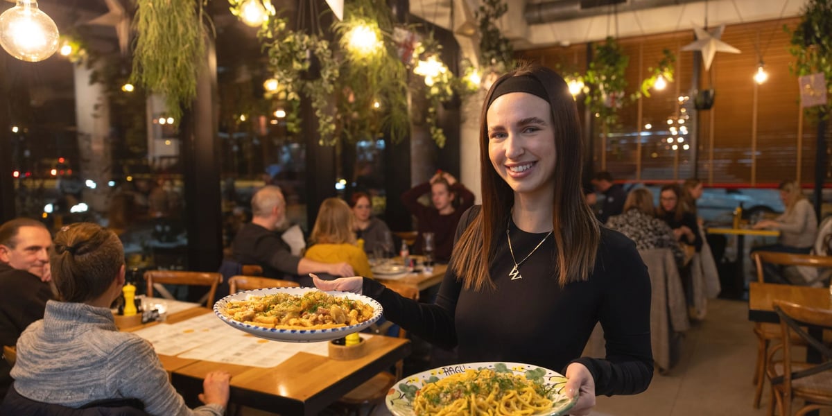 Uśmiechnięta kelnerka restauracji Ragu z dwoma talerzami z makaronami w dłoniach