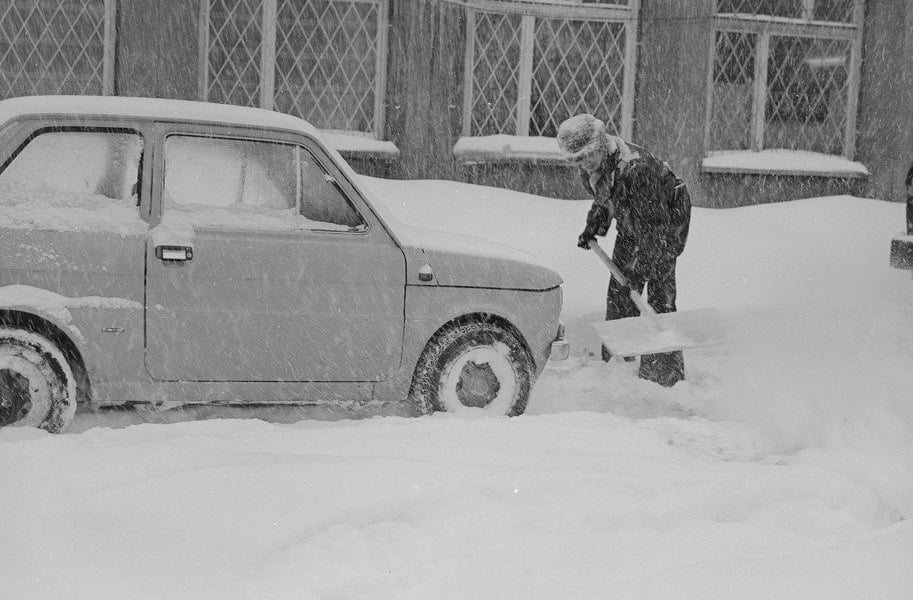 Mężczyzna z szuflą obok zasypanego śniegiem małego Fiata