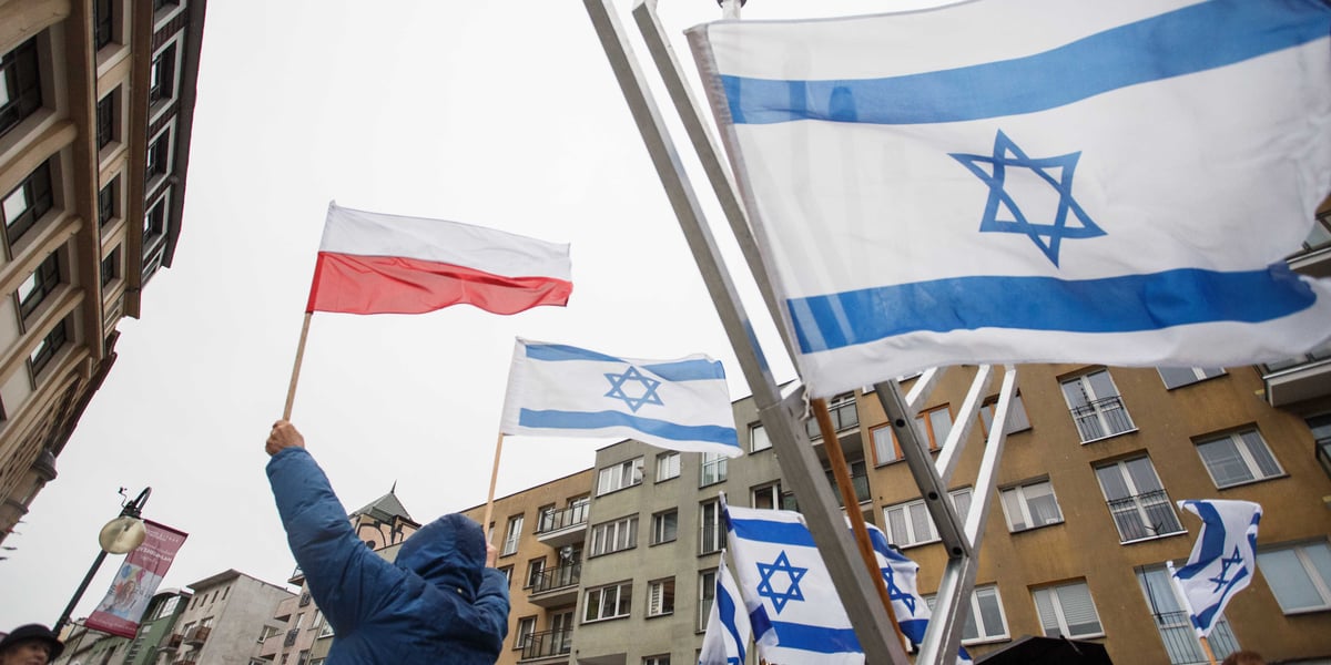 Mężczyzna wyznania mojżeszowego podnoszący nad głowę dwie flagi: Polski i Izraela. Widać także fragment tradycyjnej Chanukiji z zawieszoną flagą Izraela