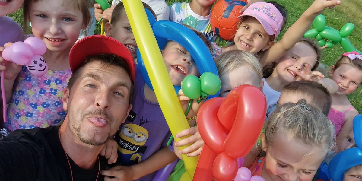Piknik osiedlowy. Na zdjęciu widać dorosłego mężczyznę i dzieci z balonami