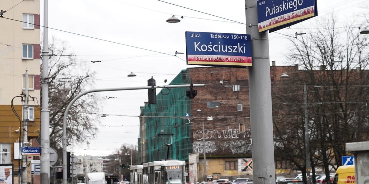 Słup z oznaczeniem ulic: Kościuszki i Pułaskiego, na dalszym planie: ulica Pułaskiego, tramwaj, auta