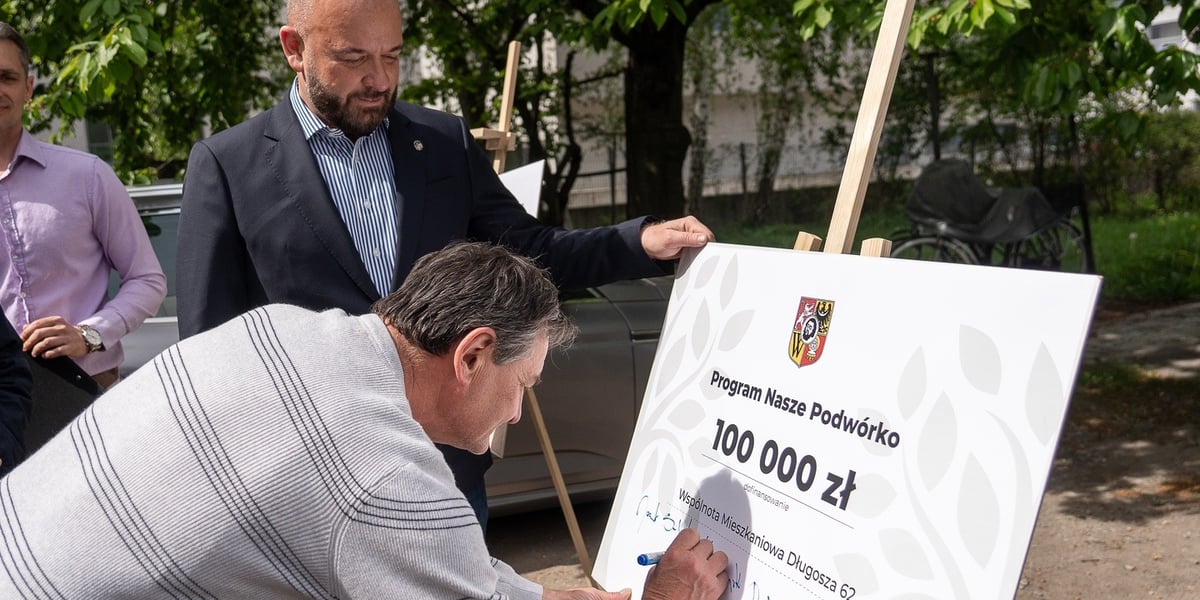 Mieszkaniec składa podpis na planszy z napisem: Program Nasze Podwórko 100 000 zł dofinansowania. Wspólnota Mieszkaniowa Długosza 62. Obok stoi prezydent Wrocławia Jacek Sutryk 