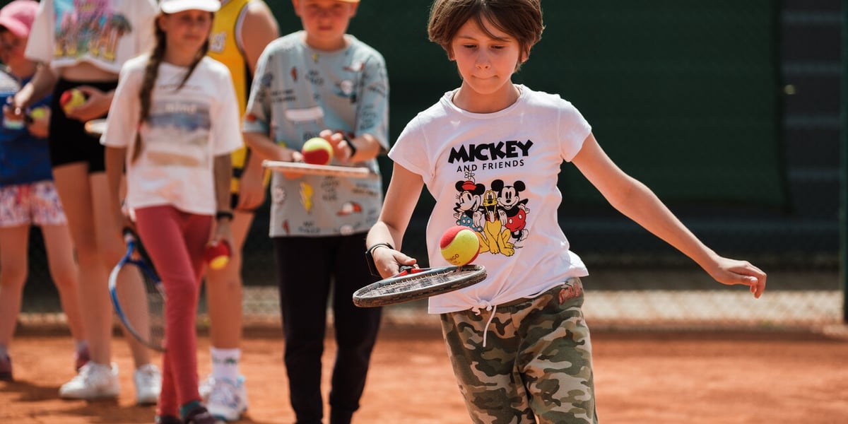 Chłopiec trzyma w dłoni rakietę tenisową, a na niej piłeczkę (Półkolonie w WCT Spartan tenis-rolki) 