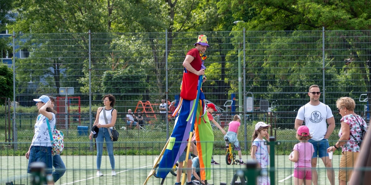 Piknik integracyjny z Kozanowie. W tle szczudlarz i bawiące się dzieci