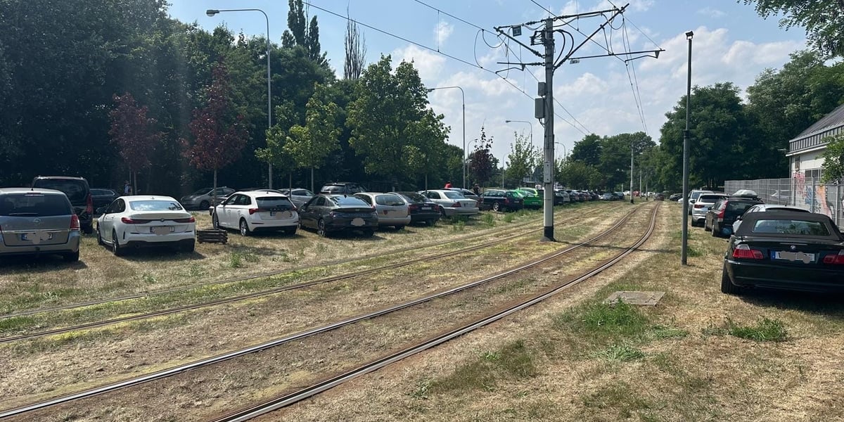 Samochody stojące na trawniku przy torowisku 