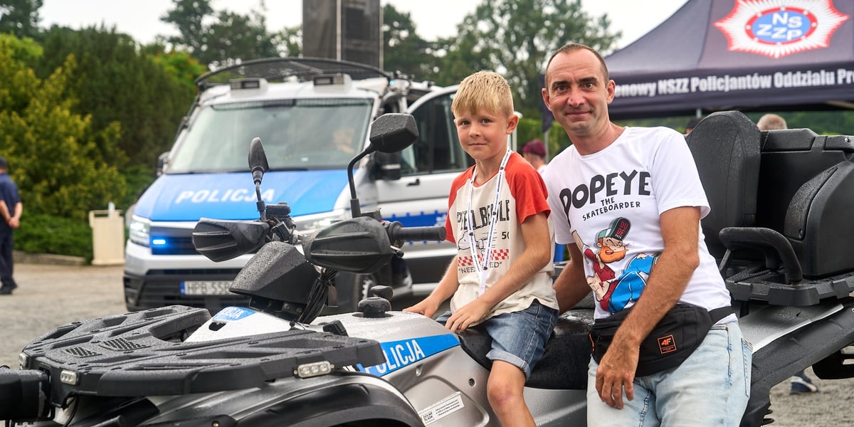 Mężczyzna i dziecko siedzą na specjalistycznych policyjnych wozach. Piknik na Pergoli z okazji 105. rocznicy powołania Policji Państwowej (22.07.2024)