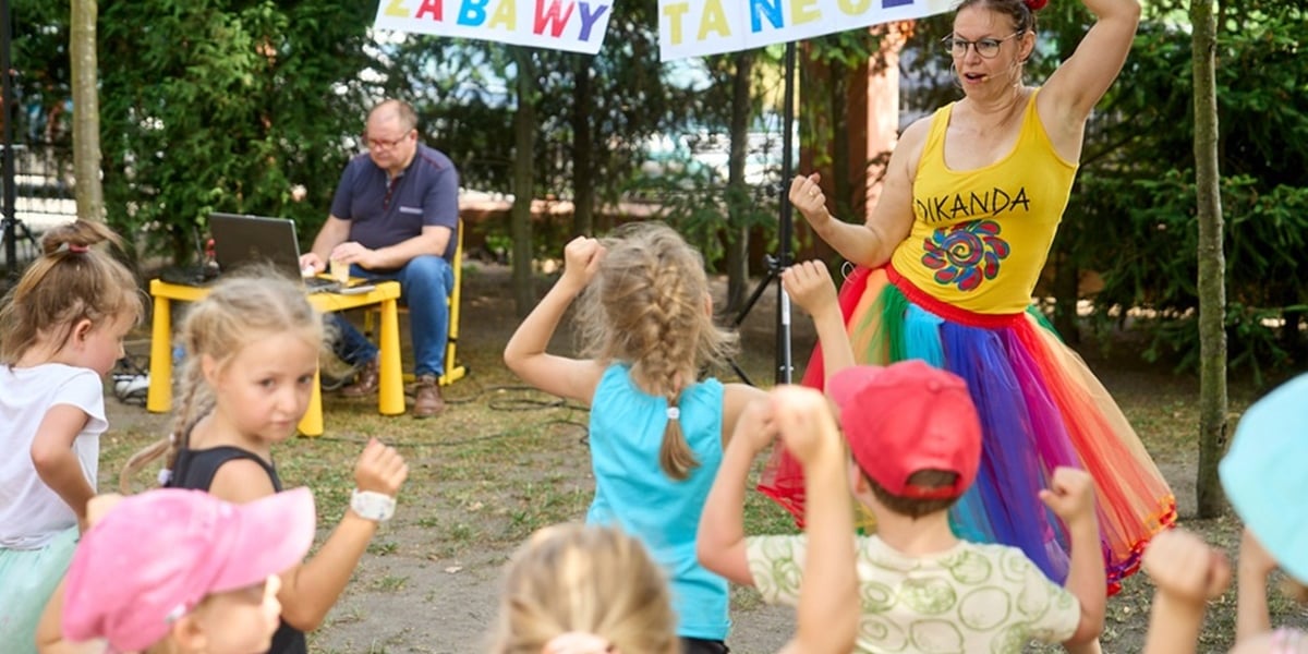 Piknik dla dzieci. Zdjęcie ilustracyjne. Na zdjęciu młoda kobieta tańczy wesoło z dziećmi