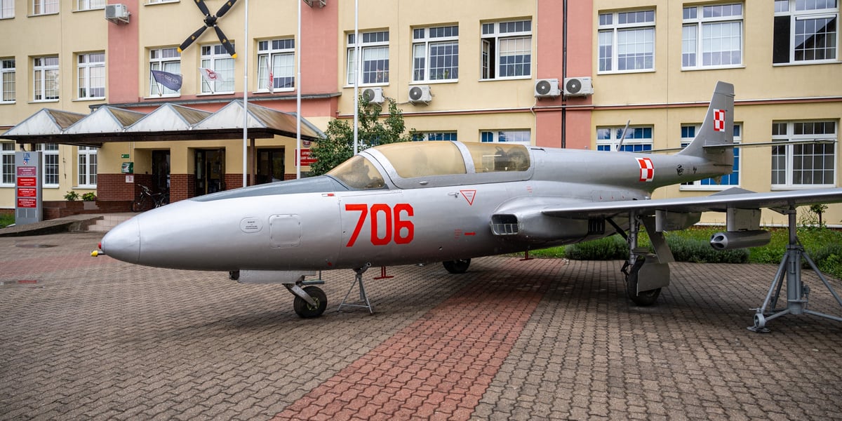 Szary samolot z czerwonym numerem 706: Iskra TS-11 przed budynkiem Lotniczych Zakładów Naukowych przy ul. Kiełczowskiej 