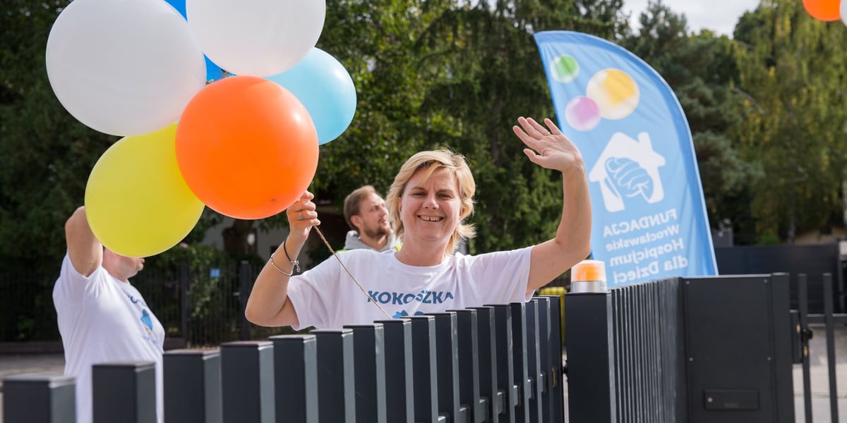 Dom opieki wytchnieniowej "KOKOSZKA" we Wrocławiu. Na zdjęciu uśmiechnięta kobieta z balonami w ręku, stojąca przy ogrodzeniu.