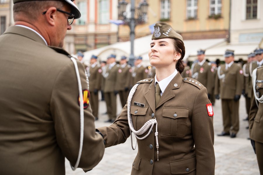 Kobieta w żołnierskim mundurze unosi głowę i ściska rękę innego żołnierza podczas uroczystości na Rynku, 15 sierpnia 2024 roku