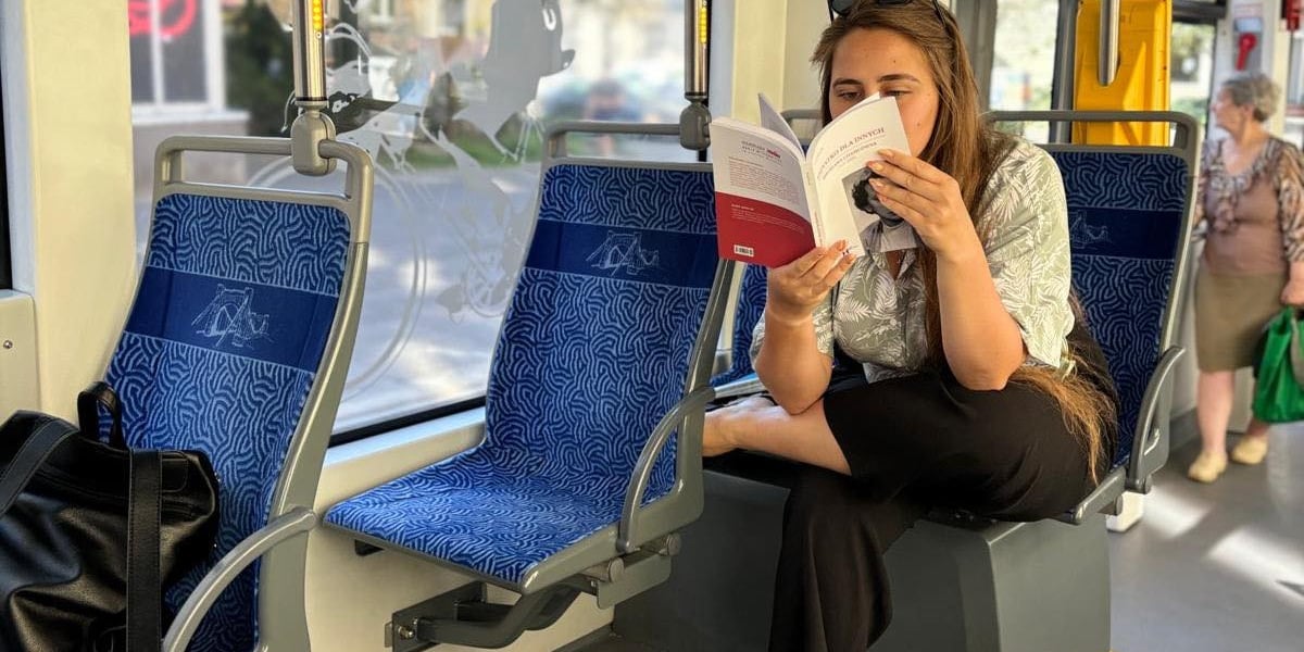 Na zdjęciu kobieta czytająca książkę w tramwaju.
