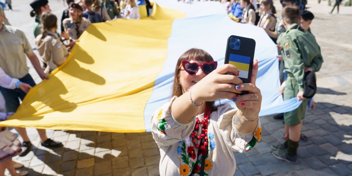 Kobieta robi zdjęcie telefonem z wielką flagą Ukrainy w tle