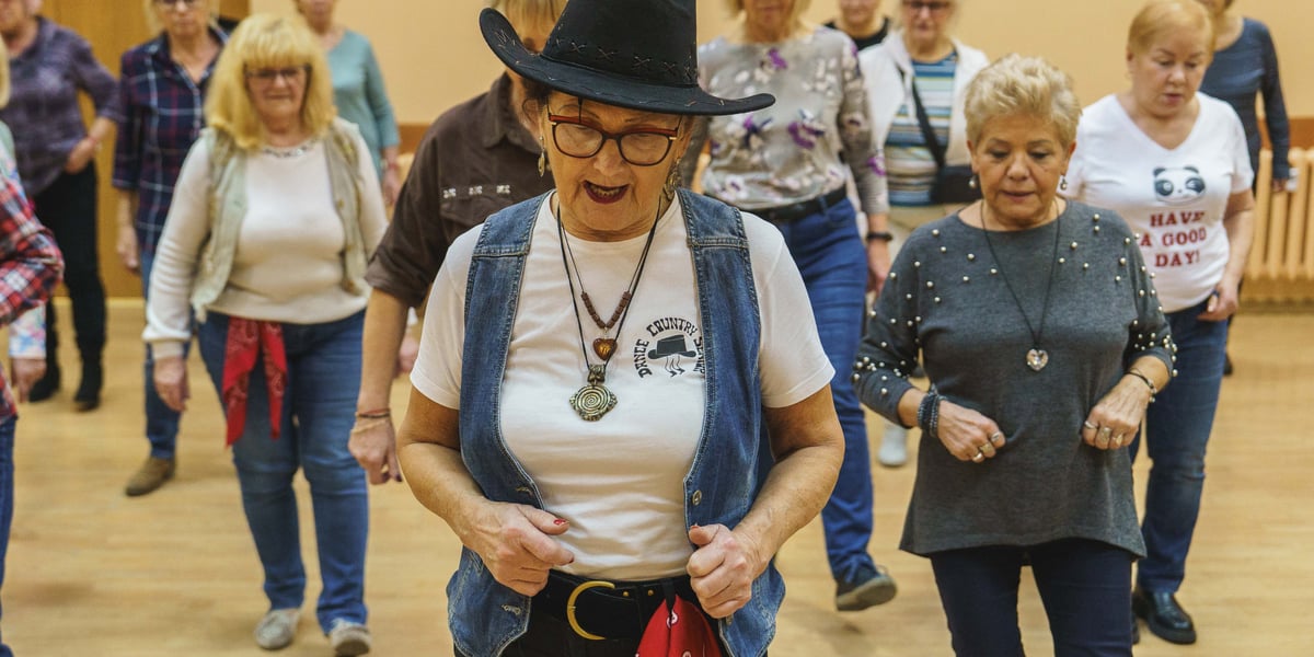 Maria Dowbecka, kierowniczka grupy tanecznej Dance Senior Country na pierwszym planie, z tyłu za tańczący seniorzy