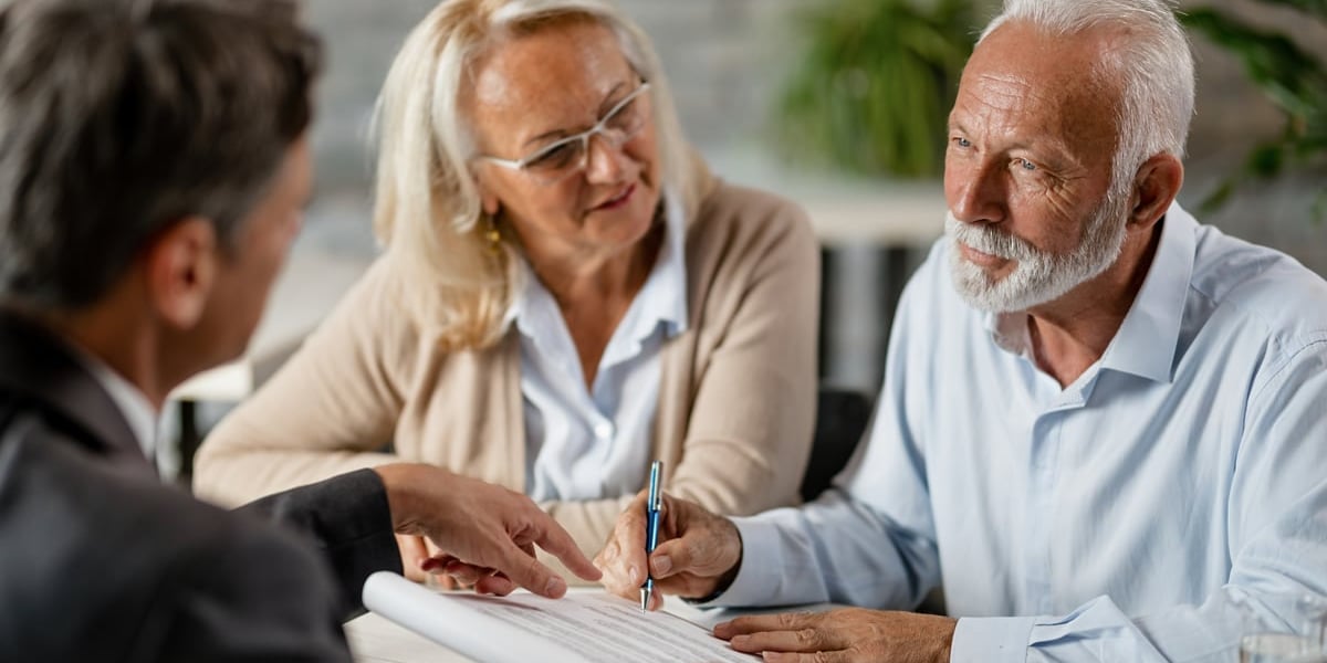 Na zdjęciu para seniorów rozmawia przy biurku z mężczyzną w garniturze