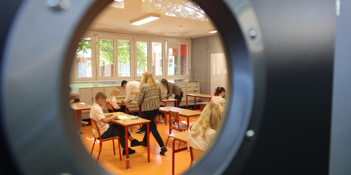 Egzamin ósmoklasisty w SP nr 29 we Wrocławiu. Przez drzwi z oddali widać uczniów siedzących w ławkach. Zdjęcie archiwalne