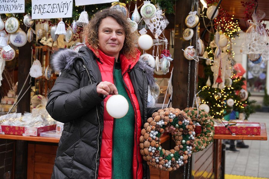 Kobieta trzymająca stroik z orzechów, stoi przed drewnianą budką na Wrocławskim Jarmarku Bożonarodzeniowym