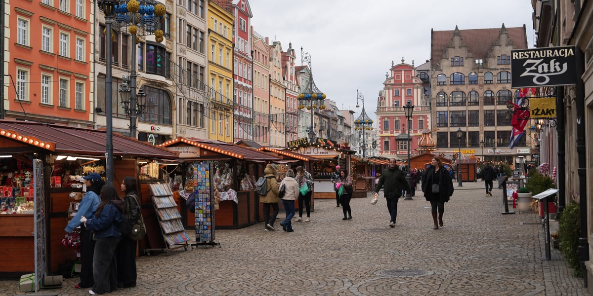 Kilka osób przechadza się po Jarmarku Bożonarodzeniowym na wrocławskim rynku.