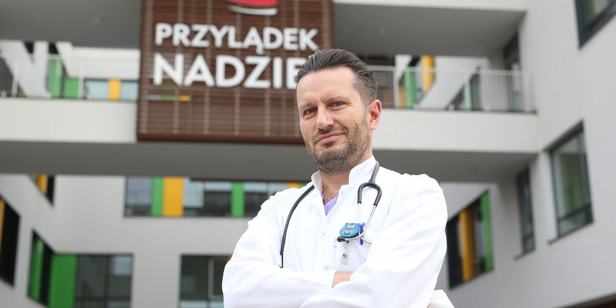 Prof. Krzysztof Kałwak, specjalista pediatrii, transplantologii klinicznej, onkologii i hematologii dziecięcej oraz immunologii klinicznej, kierownik Katedry i Kliniki Transplantacji Szpiku, Onkologii i Hematologii Dziecięcej Uniwersytetu Medycznego we Wrocławiu. Na zdjęciu mężczyzna ze stetoskopem na tle budynku z szyldem Przylądek Nadziei