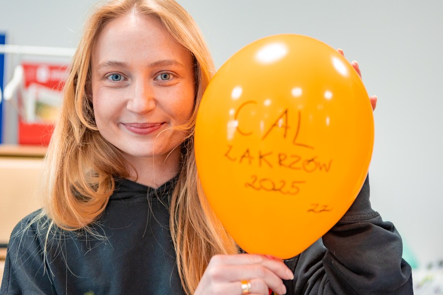 Młoda uśmiechnięta dziewczyna z żółtym balonem z napisem CAL Zakrzów 2025