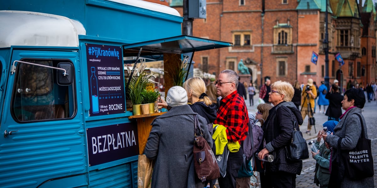 Kolejka osób ustawiona przed samochodem o nazwie "watertruck", który serwuje wodę