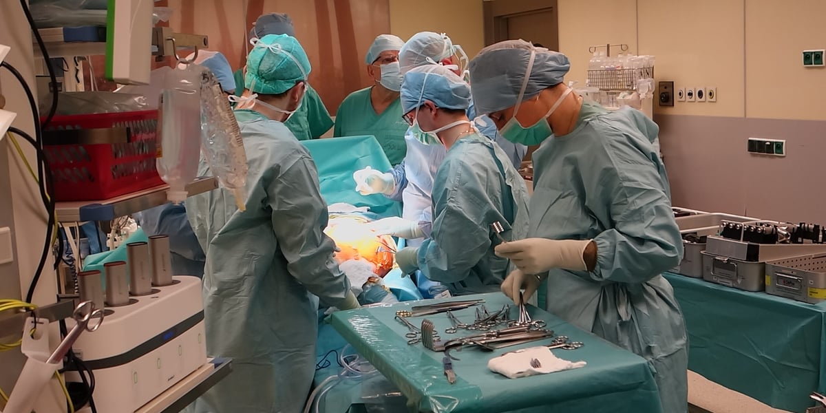 Na zdjęciu sala operacyjna. Przy stole operacyjnym stoi kilka osób w fartuchach