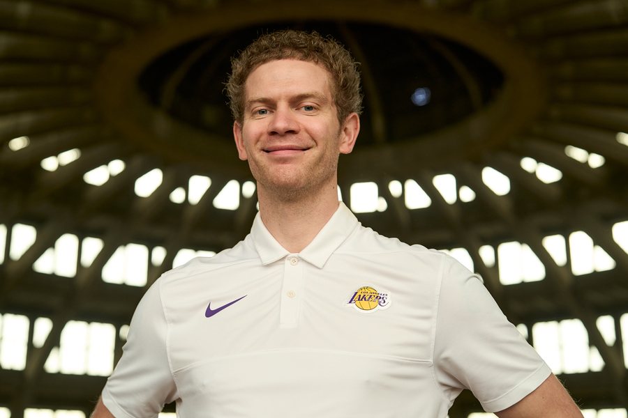 Uśmiechnięty Bronek w białej koszulce z logo Lakersów, na tle kopuły Hali Stulecia