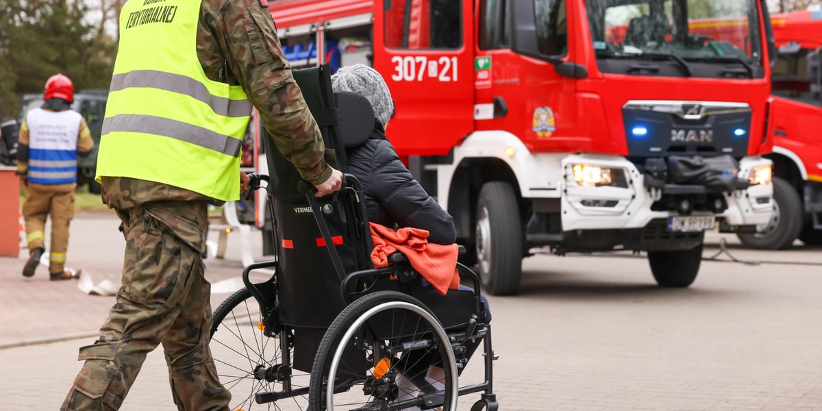 Żołnierz pcha osobę na wózku podczas akcji ewakuacyjnej