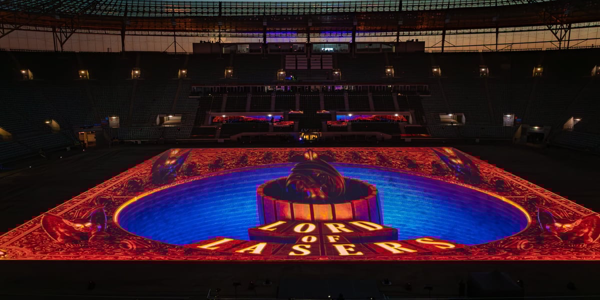 Kolorowe iluminacje na płycie stadiony z napisem "Lord of Lasers"