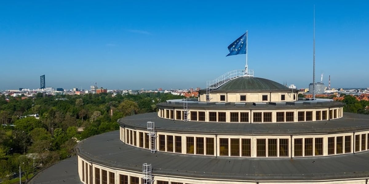 Kopuła Hali Stulecia z flagą unijną. Na zdjęciu na dachu dużej budowli powiewa niebieska flaga