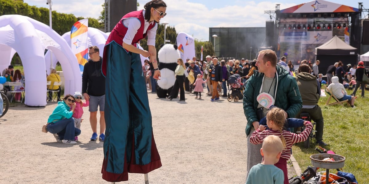 Piknik na Pergoli z okazji Dni Funduszy Europejskich. Na zdjęciu dziewczyna na szczudłach bawi się z dzieckiem i mężczyzną