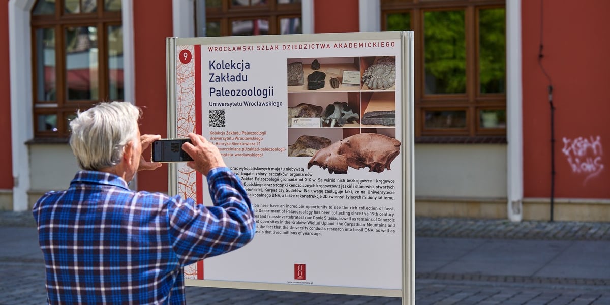 Plenerowa wystawa "Wrocław na szlaku dziedzictwa akademickiego" przy ul. Kuźniczej. Na zdjęciu mężczyzna przed tablicą informującą o jednym z muzeów