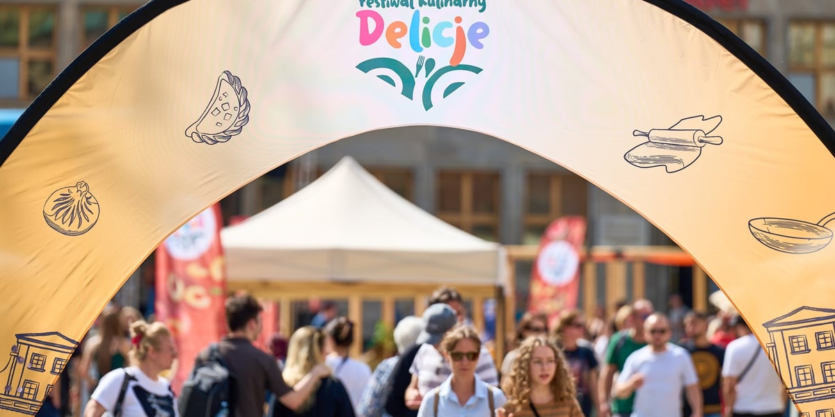 Tłum ludzi pod łukiem dekoracyjnym z napisem Delicje