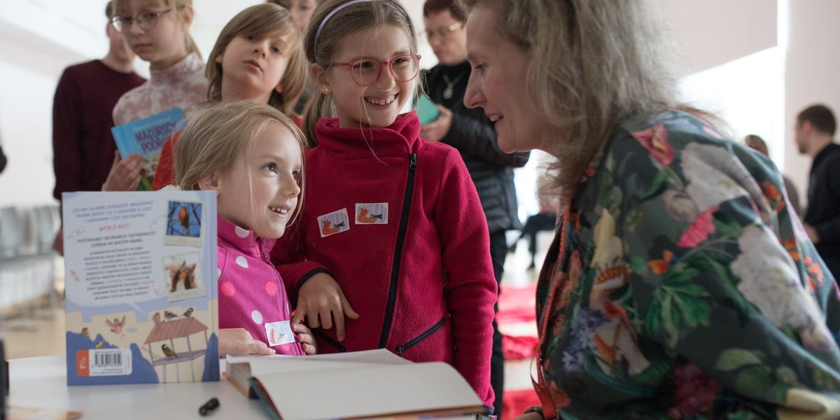 Zdjęcie ilustracyjne: jedna z poprzednich edycji Międzypokoleniowego Festiwalu Literatury Dziecięcej Ojce i Dziatki. Na zdjęciu dzieci rozmawiające z uśmiechniętą kobietą.