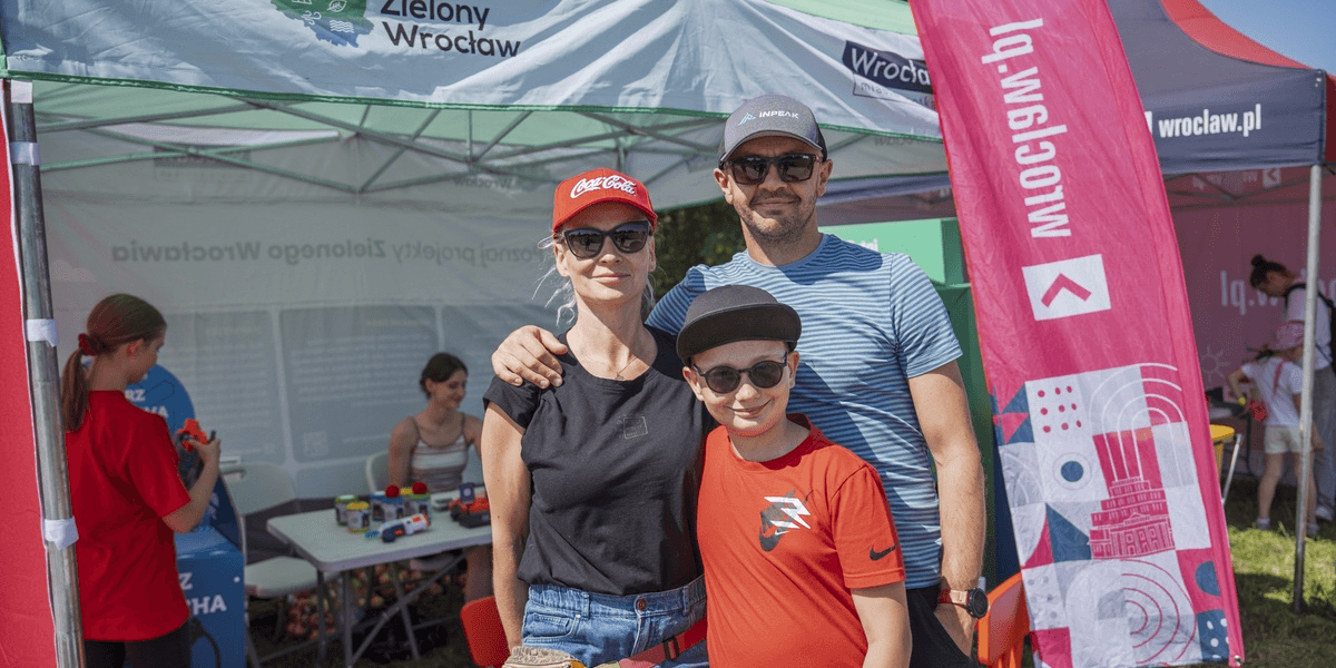 Uczestnicy Festiwalu Pasibrzucha na Partynicach. Na zdjęciu uśmiechnięta rodzina, w tle stanowiska Wroclaw.pl i Zielonego Wrocławia