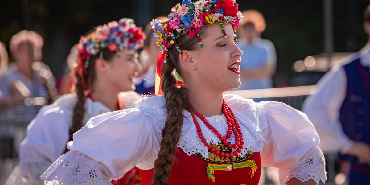 Dwie kobiety w wiankach na głowach i strojach ludowych, w tańcu na pl. Wolności