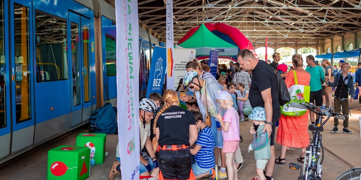 Piknik Bezpieczeństwa w zajezdni na Borku, 28 czerwca 2025, pokaz pierwszej pomocy w hali zajezdni, na zdjęciu uczestnicy wydarzenia oraz ratowniczka medyczna