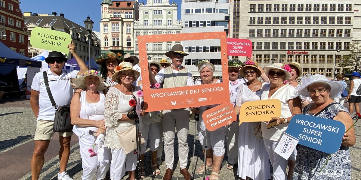 Wrocławscy seniorzy na placu Solnym z Rynku, trzymają pomarańczową ramkę z napisem Wrocławskie Dni Seniora 