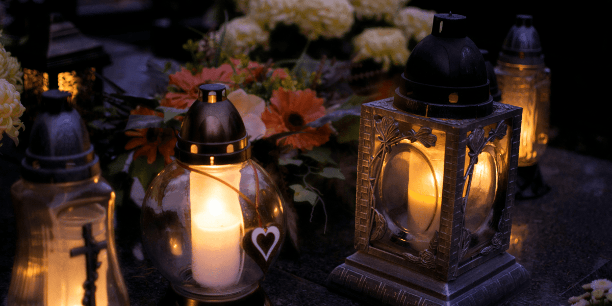 Zdjęcie ilustracyjne: zapalone znicze na grobie, w tle chryzantemy