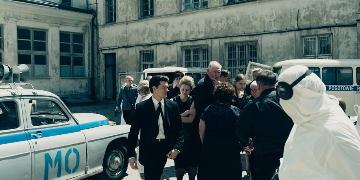 Kadr z serialu "Czarna śmierć". Na zdjęciu widać grupę osób ubranych na czarno oraz osobę w odzieży ochronnej i okularach