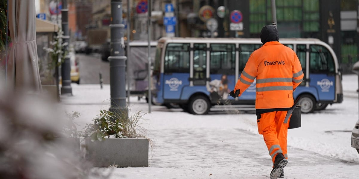 Pierwszy śnieg we Wrocławiu, 24.11.2025. Pracownik z pomarańczowym kombinezonie posypujący solą chodnik.