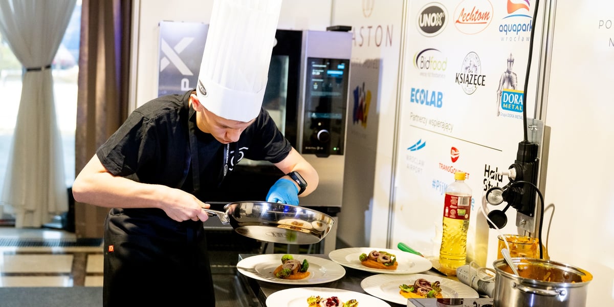 X Wrocławski Kulinarny Rajd Młodych Mistrzów  we Wrocławiu. Na zdjęciu skupiony młody człowiek w czapce kucharskiej przygotowuje danie.