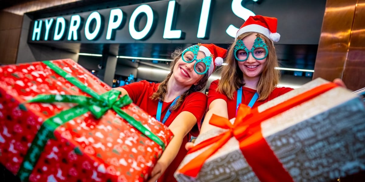 Hydropolis zaprasza na swoje 10 urodziny. Na zdjęciu uśmiechnięte dziewczyny trzymają prezenty na tle napisu Hydropolis