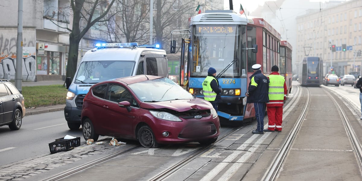 Wypadek - rozbity samochód na torach tramwajowych, za nim tramwaj, z przodu pracownicy służb
