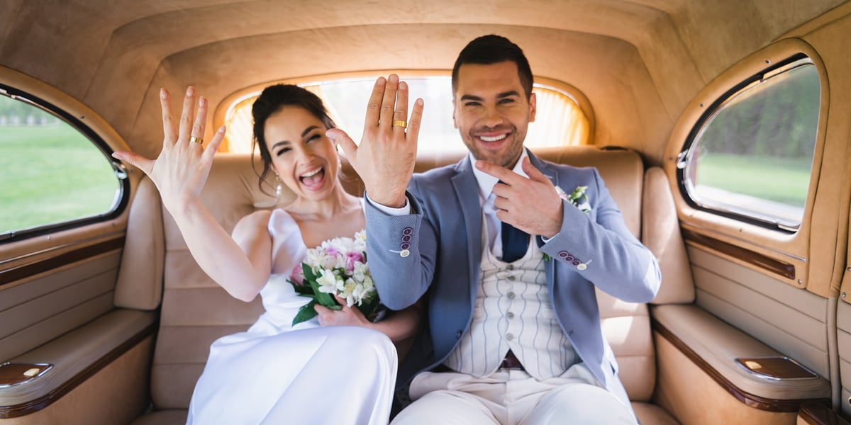 Na zdjęciu młoda para we wnętrzu luksusowego samochodu pokazuje obrączki na dłoniach. Zdjęcie ilustracyjne