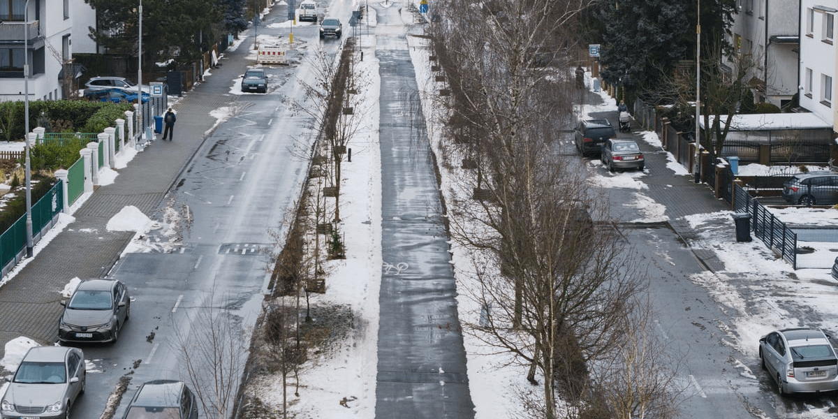 Widok z lotu ptaka na ścieżkę rowerową między zaśnieżonymi psami zieleni przy Alei Piastów na Oporowie.